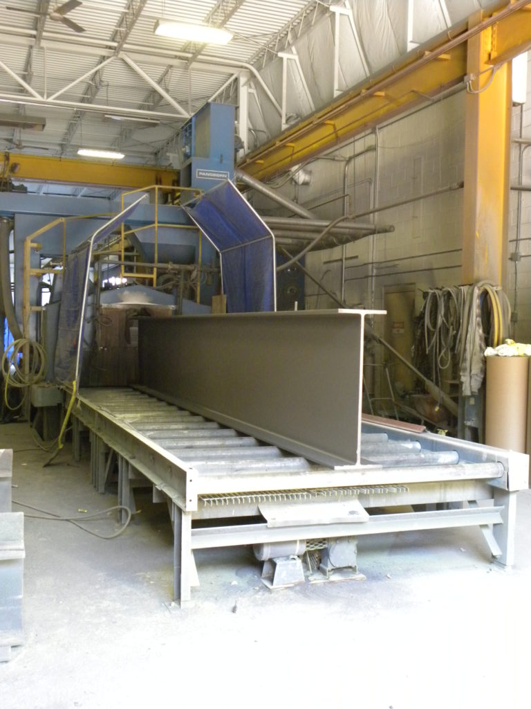 a large silver metal I-beam emerges from the Rotoblast wheel machine fully cleaned