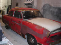 a vintage car with damaged red paint is prepped for plastic media blasting