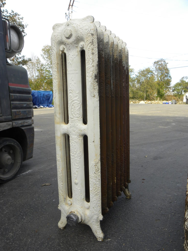 a decorative steam radiator shown prior to restoration with rusted areas and yellowed, chipping white paint