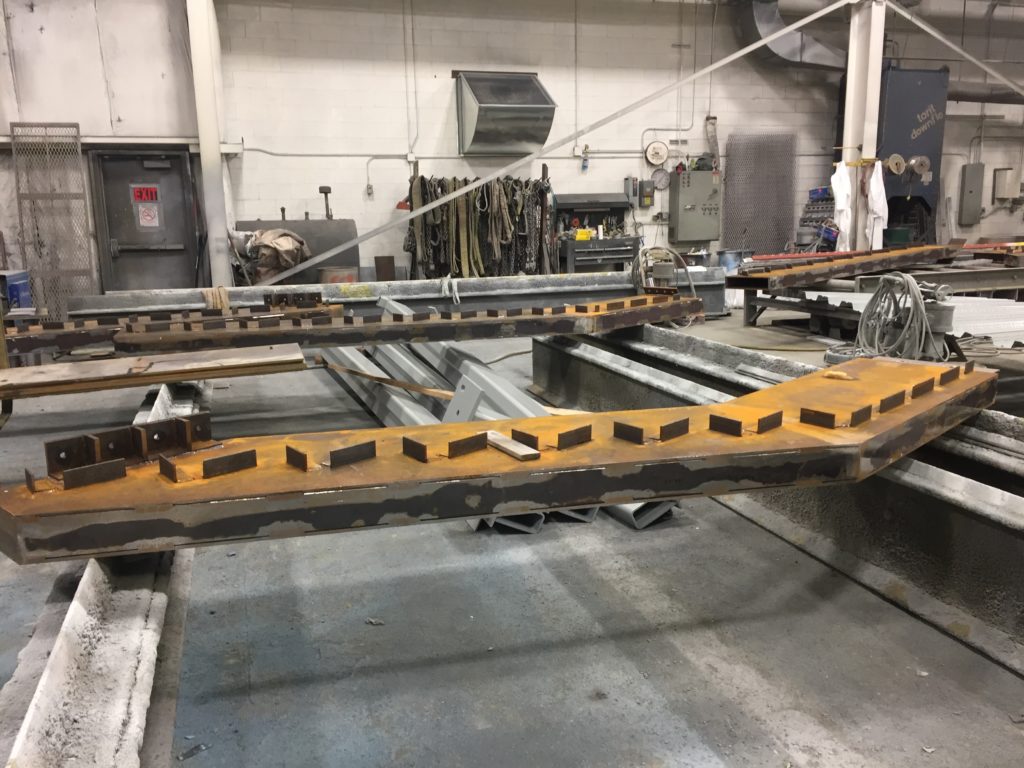 orange rusted steel support beams are laid out in the Inter-City Contracting facility in preparation for the AESS process