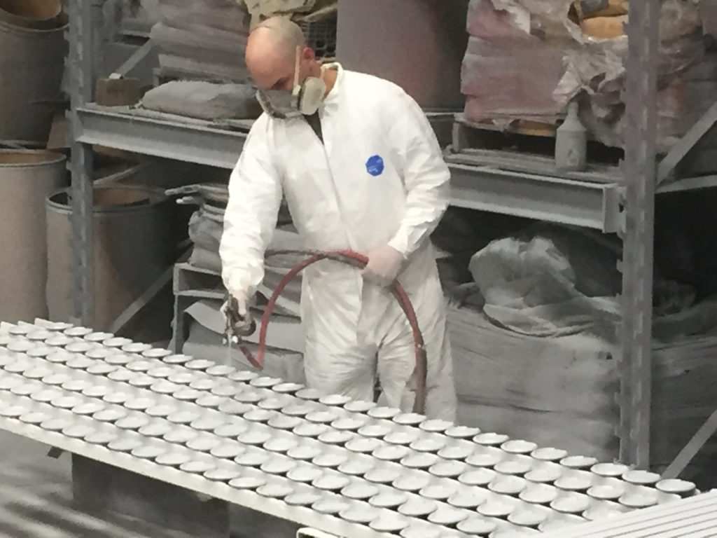 an Inter-City Contracting employee applies a white sprayed coating to a piece of sculptural steel covered in round scales