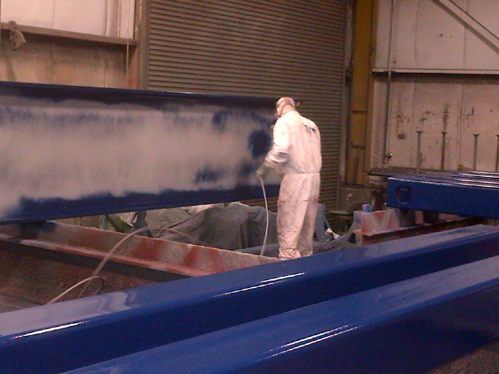 an Inter-City Contracting employee applies a royal blue spray coating to a large steel beam